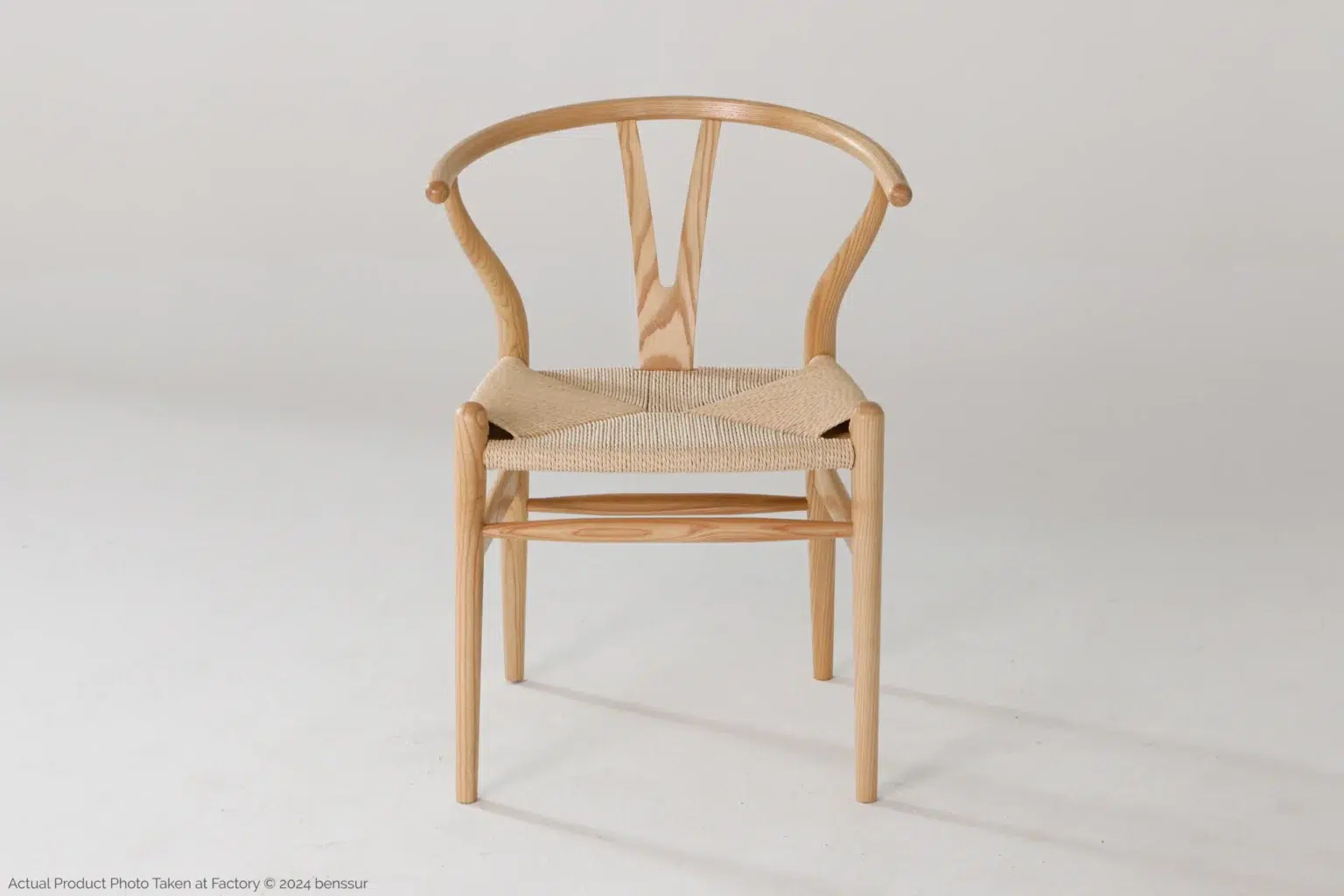 Hans Wegner_Wishbone Chair_Replica_Paper Rope_Natural_Ash_Front A wooden chair with a curved backrest and woven seat, photographed against a plain white background. The design is minimalist and modern.