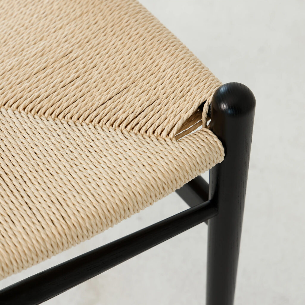 Close-up of a woven straw seat on a black wooden chair, showing a damaged corner where some of the weaving has come undone, exposing the underlying frame.