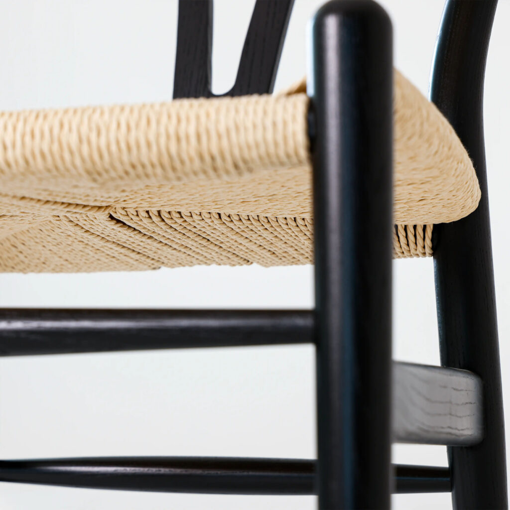 Close-up of a chair showing a woven natural-coloured seat and black wooden legs and frame, highlighting the texture of the seat and the smooth finish of the wood.