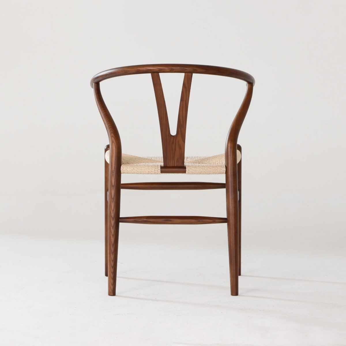 Wishbone Chair_Dark_B2 A wooden chair with a curved backrest, Y-shaped central support, and a woven seat, photographed against a plain white background.