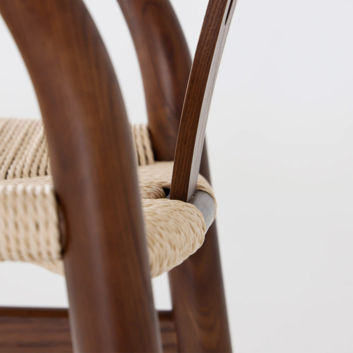 Wishbone Chair_Dark_B3 Close-up of a wooden chair with smoothly curved dark wood legs and a woven natural fibre seat, showing the detailed craftsmanship and texture of the materials.