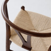 Close-up of a wooden chair with a curved backrest and a woven, light-coloured seat. The chair has a minimalist, elegant design and is placed on a white surface.