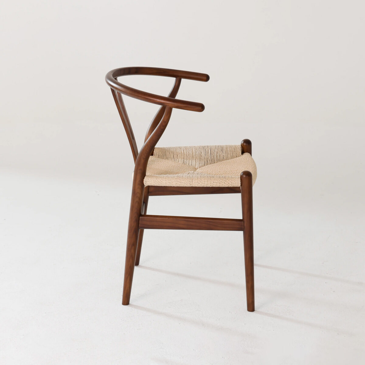 Wishbone Chair_Dark_B7 A modern wooden chair with a curved backrest and a woven seat, shown against a plain white background. The design features smooth lines and a minimalist, Scandinavian style.