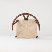 A modern wooden chair viewed from above, featuring a woven beige seat and elegantly curved wooden armrests, set against a plain light background.