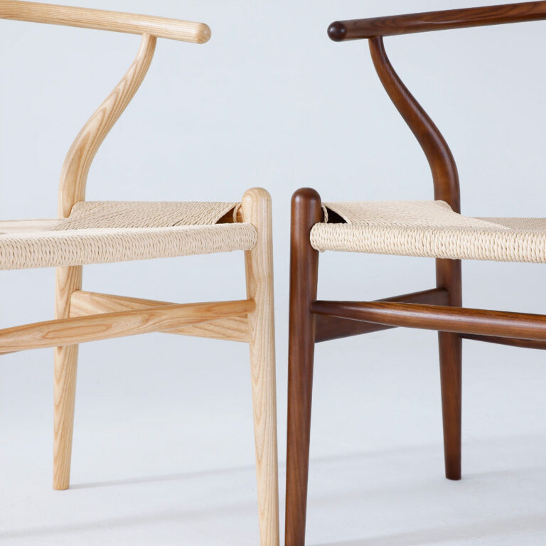 Two wooden chairs with woven seats are placed side by side. One chair is light wood, the other dark, both featuring curved backrests and minimalist, modern design.