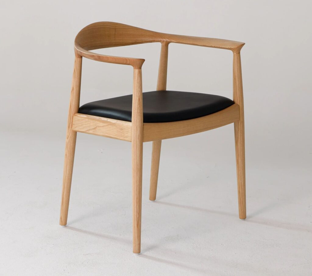 A modern wooden chair with a curved backrest, slender legs, and a black cushioned seat, set against a plain light background.