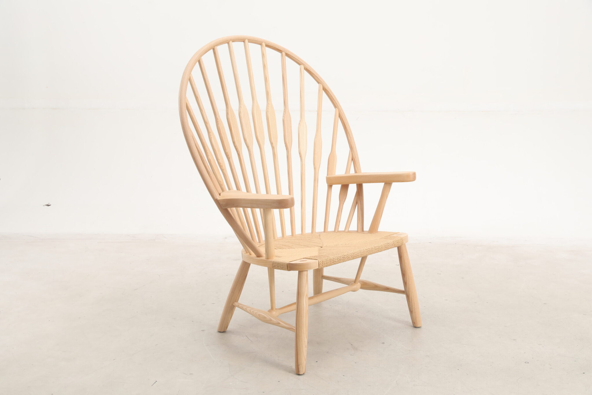 A wooden chair with a high, rounded spindle back, wide armrests, and a woven seat, set against a plain white background.
