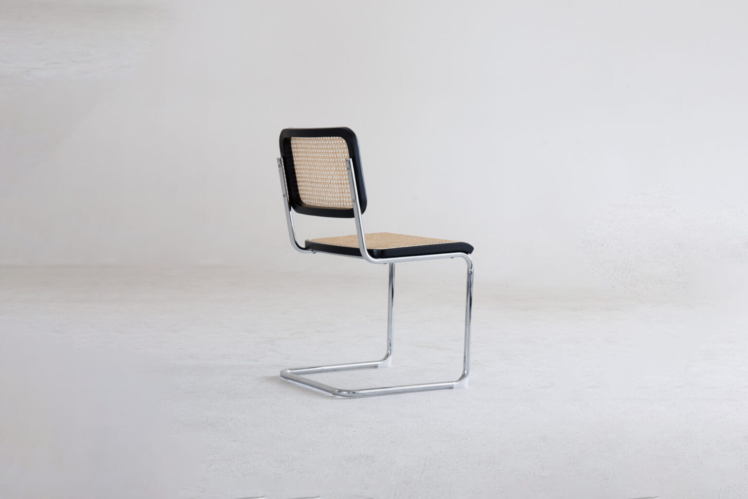 Back side view A modern chair with a chrome cantilever frame, a cane-woven backrest, and a matching cane seat, positioned on a light, minimalist background.