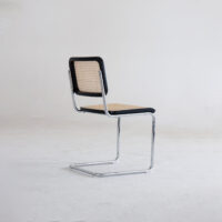 A modern chair with a chrome cantilever frame, a cane-woven backrest, and a matching cane seat, positioned on a light, minimalist background.