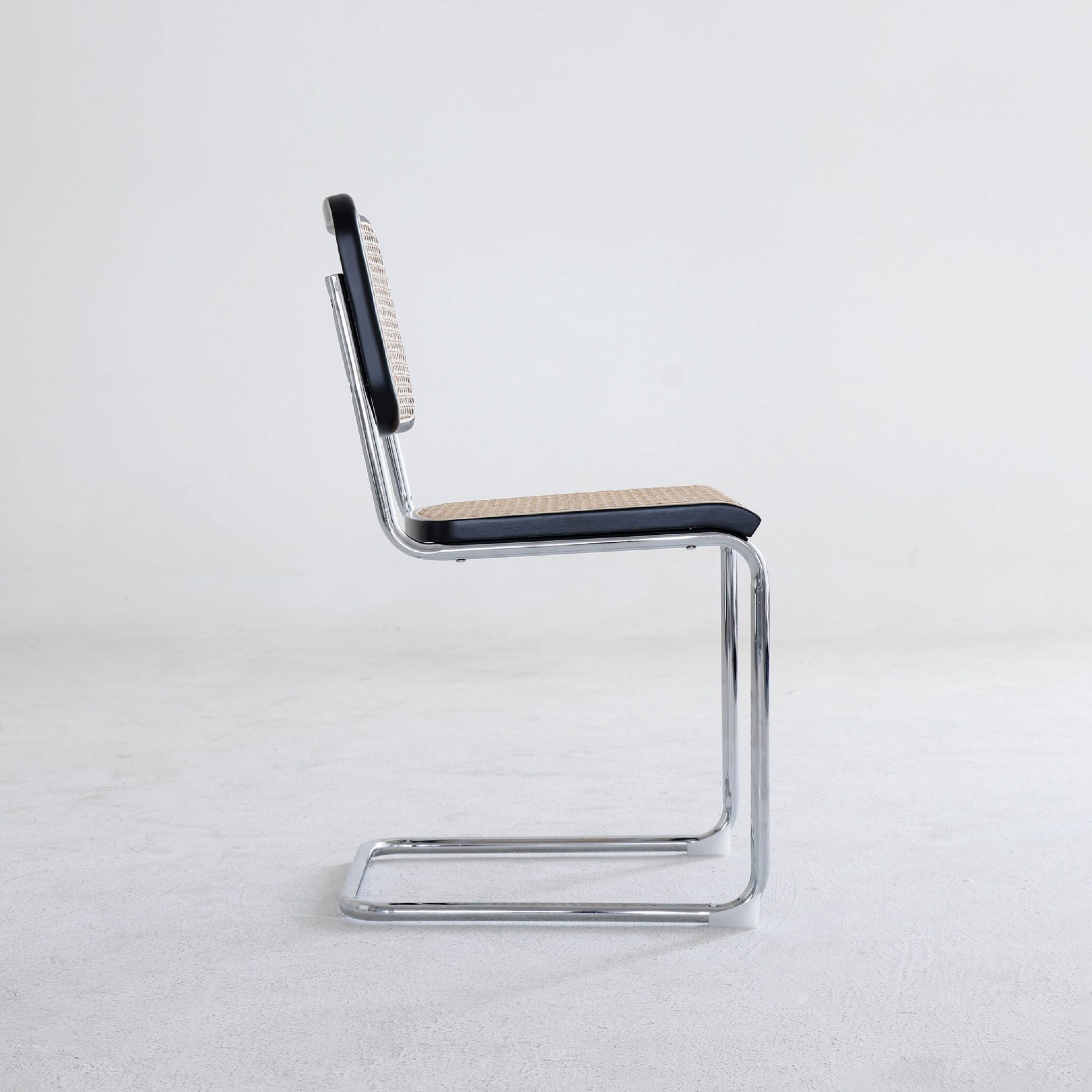 A modern cantilever chair with a chrome frame, woven rattan backrest, and seat, viewed from the side against a plain white background.