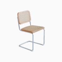 A modern chair with a chrome cantilever frame, light wood accents, and a woven cane seat and backrest, set against a plain white background.