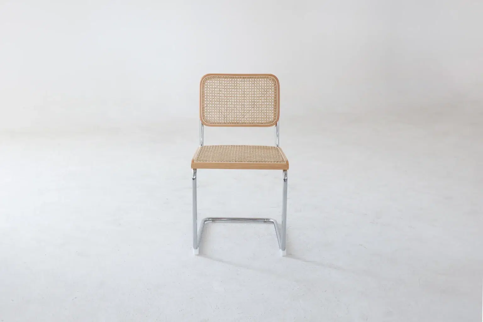 Front view A single chair with a chrome frame and a woven cane seat and backrest sits on a plain white floor against a blank white background.