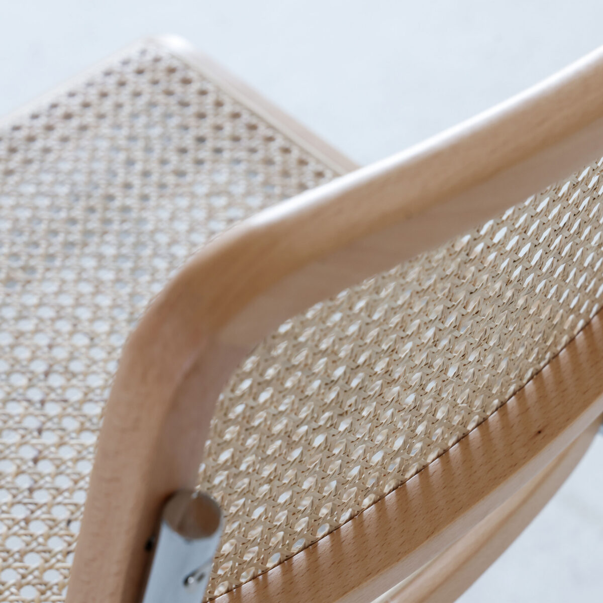Natural Frame_Chrome_B1 Close-up of a wooden chair with a woven cane seat and backrest, featuring a light, natural finish. The image highlights the texture and pattern of the cane weaving and the smooth, curved wood frame.