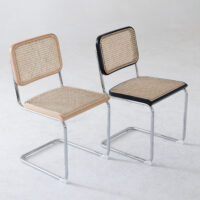 Two modern chairs with chrome cantilever frames, rattan seat and backrests. One chair has natural wood edges, the other has black edges. Both are set on a plain light-coloured floor with a neutral background.