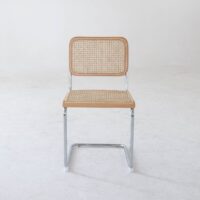 A chair with a chrome metal frame, a woven cane seat and backrest, and light wood accents, placed on a plain white floor against a white wall.