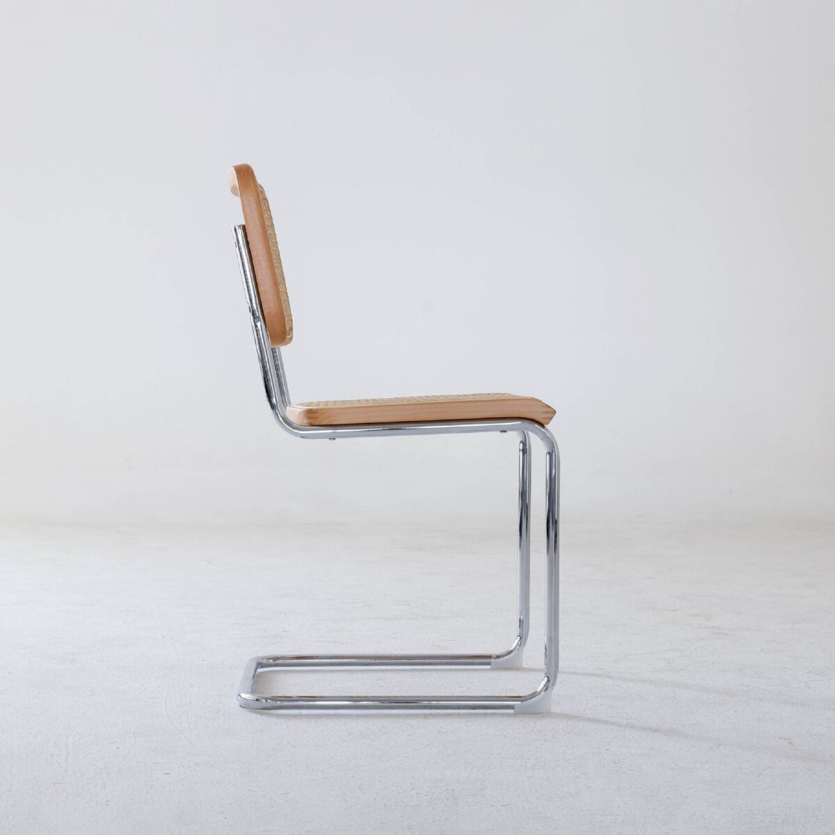 Natural Frame_Chrome_B6 A side view of a modern chair with a chrome cantilever frame and tan leather seat and backrest, set against a plain white background.