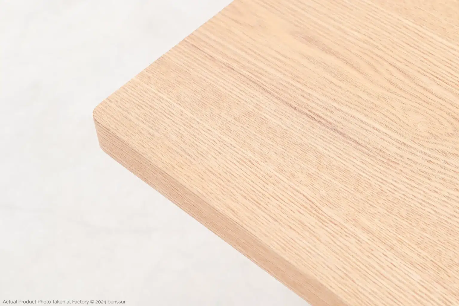 Jean Prouvé_S.A.M No.502 Table_Replica_Natural_Ash_Detail_1 A close-up of the corner of a light-coloured wooden tabletop, showing its smooth surface and natural wood grain pattern against a pale background.