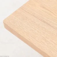 A close-up of the corner of a light-coloured wooden tabletop, showing its smooth surface and natural wood grain pattern against a pale background.