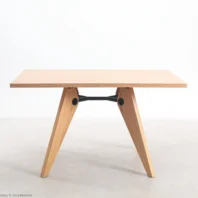 A minimalist wooden table with a rectangular top and two V-shaped legs connected by a black metal support bar, set against a plain white background.