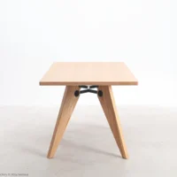 A minimalist wooden table with a square top and angled, V-shaped legs, connected by a black metal support bar, set against a plain white background.