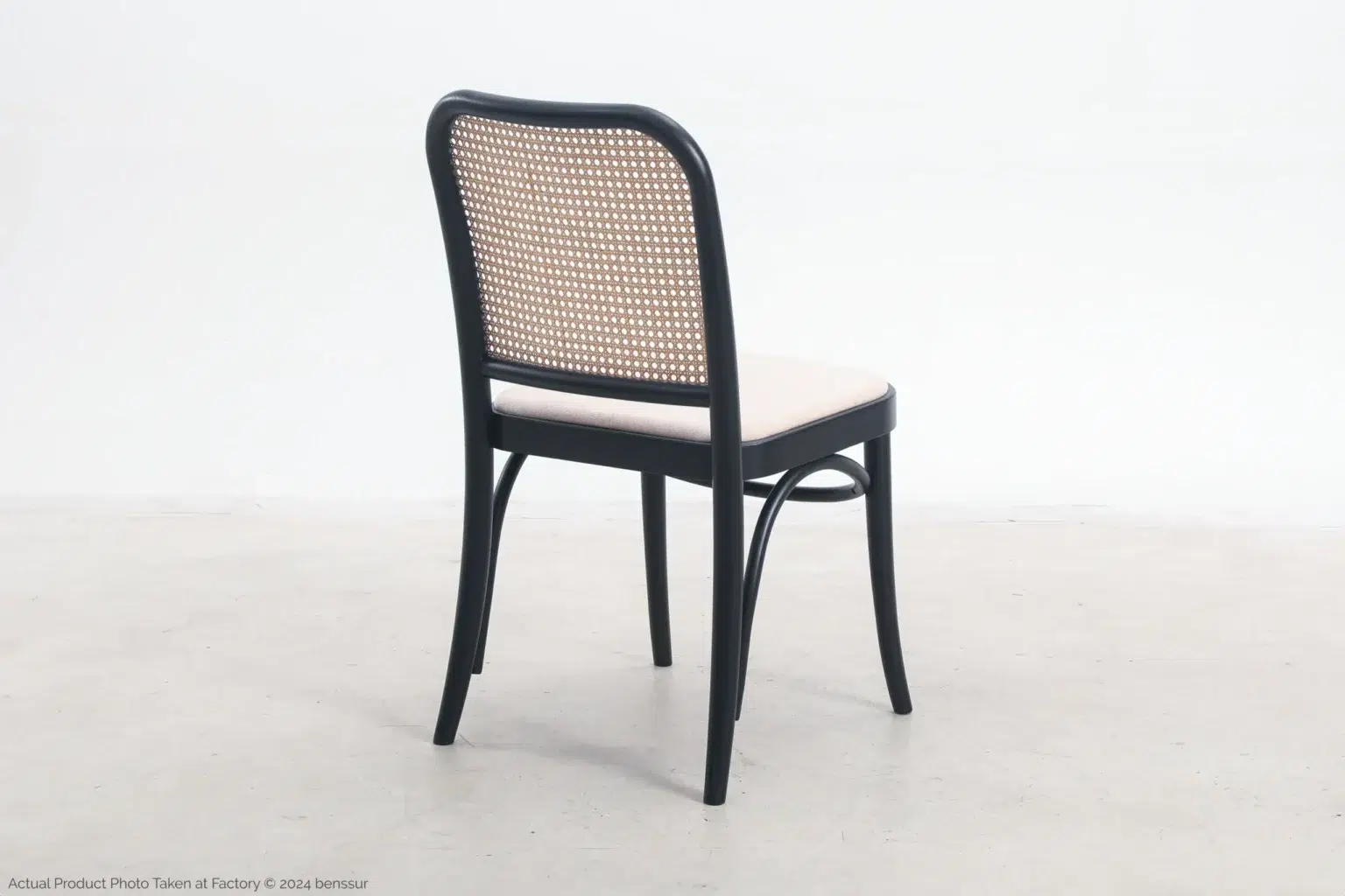 Josef Hoffmann_No811 Chair_Replica_Upholstered_Black_Ash_Back Right A wooden chair with a black frame, woven cane backrest, and light-coloured cushioned seat, placed on a light grey floor against a white background.