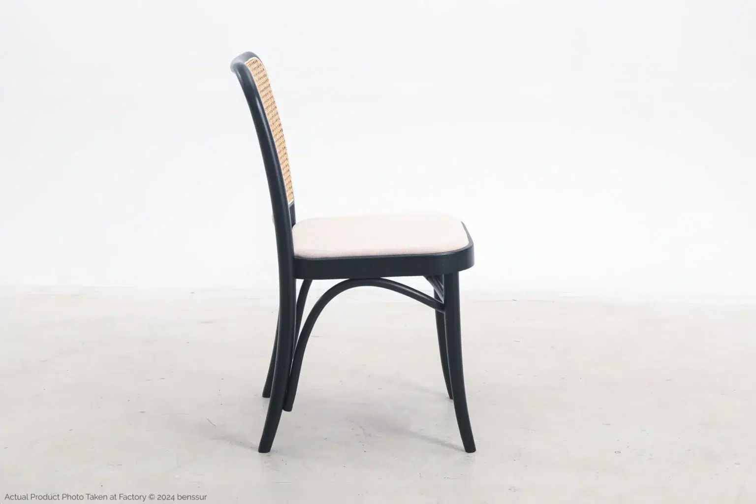 Josef Hoffmann_No811 Chair_Replica_Upholstered_Black_Ash_Right A side view of a simple chair with a black wooden frame, light-coloured cushioned seat, and woven rattan backrest, placed on a plain light floor against a white background.