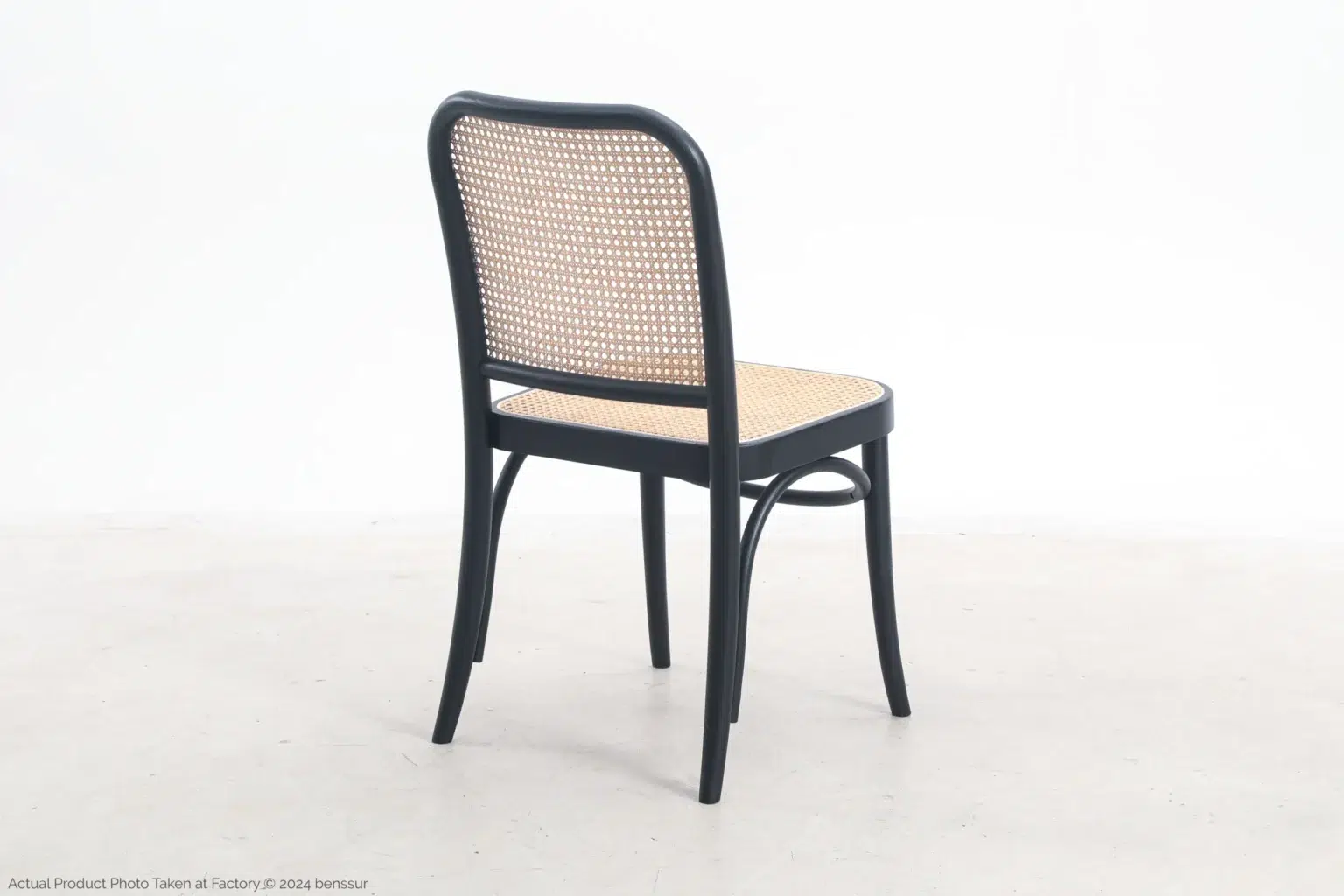 Josef Hoffmann_No811 Chair_Replica_Woven Caning_Black_Ash_Back Right A wooden chair with a black frame, curved legs, and a woven cane seat and backrest is placed on a light-coloured floor against a plain white background.