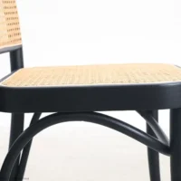 A close-up side view of a chair with a woven cane seat and backrest, featuring a black wooden frame and curved legs, against a plain white background.