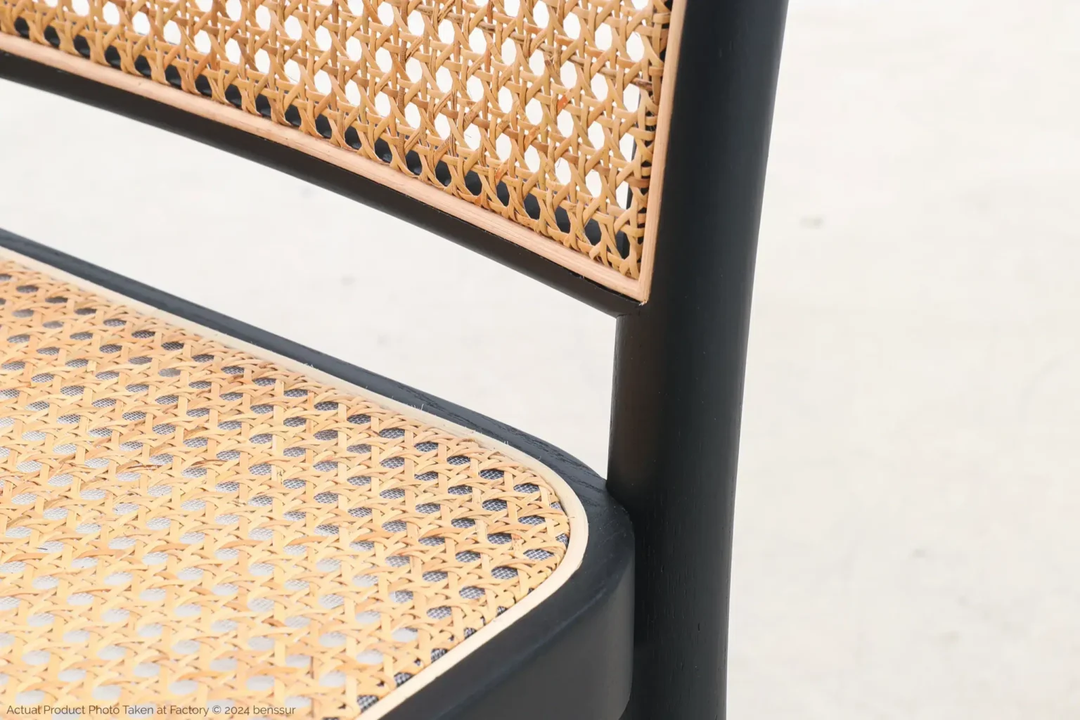 Josef Hoffmann_No811 Chair_Replica_Woven Caning_Black_Ash_Detail_4 Close-up of a chair with a woven cane seat and backrest, framed by a smooth, black wooden structure. The background is plain and light-coloured.