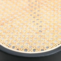 Close-up of a woven cane or rattan seat with a light natural finish and black wooden frame, showing the detailed criss-cross pattern of the weaving.