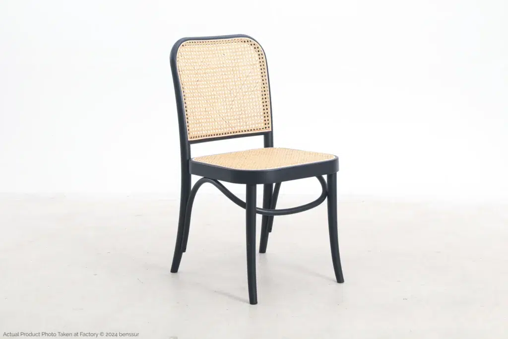 A wooden chair with a black frame and light-coloured woven cane backrest and seat, positioned on a plain light floor against a white background.