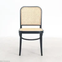 A black wooden chair with a woven cane seat and backrest, positioned on a light-coloured floor against a plain white background.