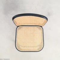 Top-down view of a chair with a woven cane seat and backrest, featuring a black frame, placed on a light, smooth surface.