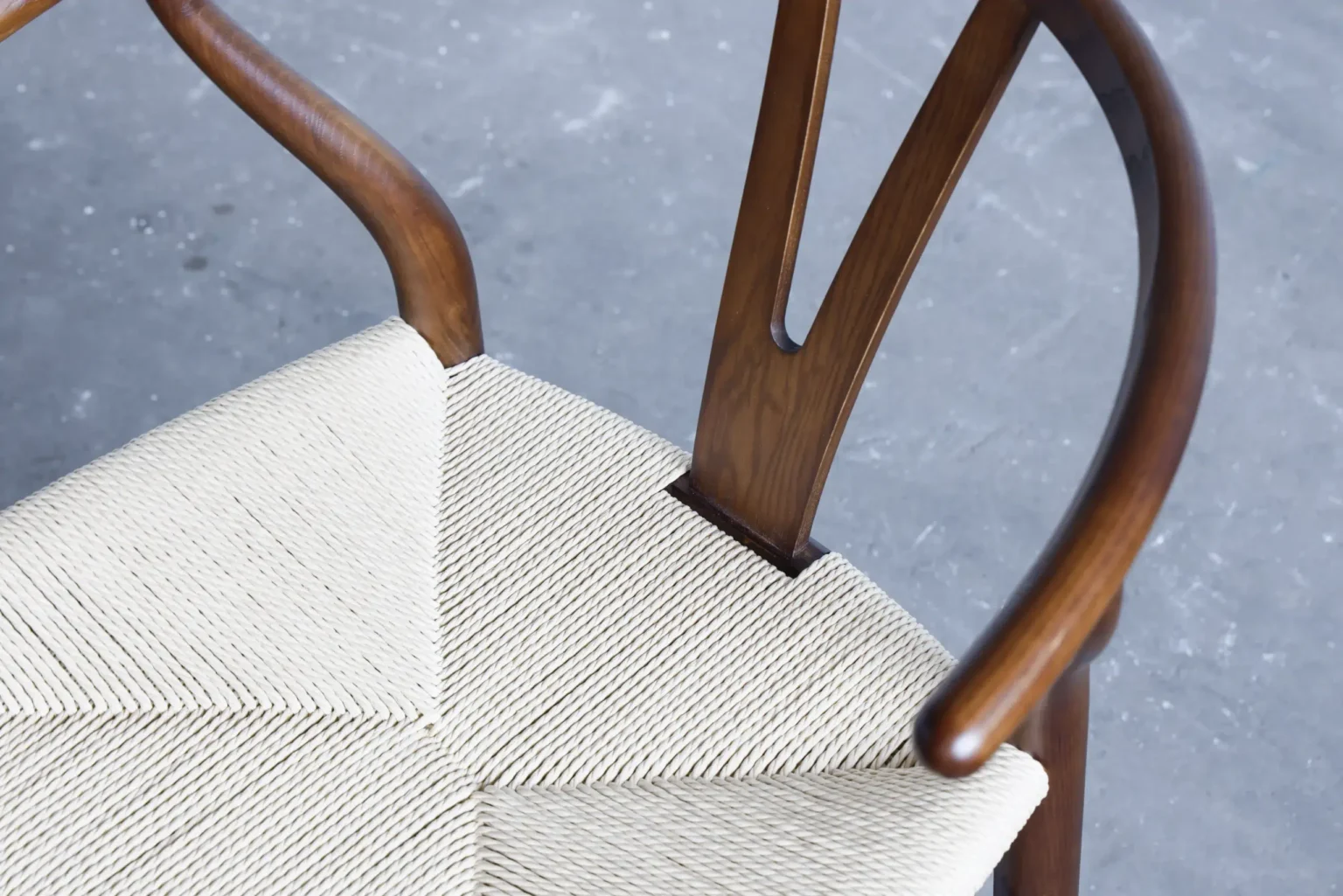 12 A close-up view of a wooden chair with curved armrests and a woven, light-coloured seat on a grey, textured floor.