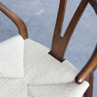 A close-up view of a wooden chair with curved armrests and a woven, light-coloured seat on a grey, textured floor.