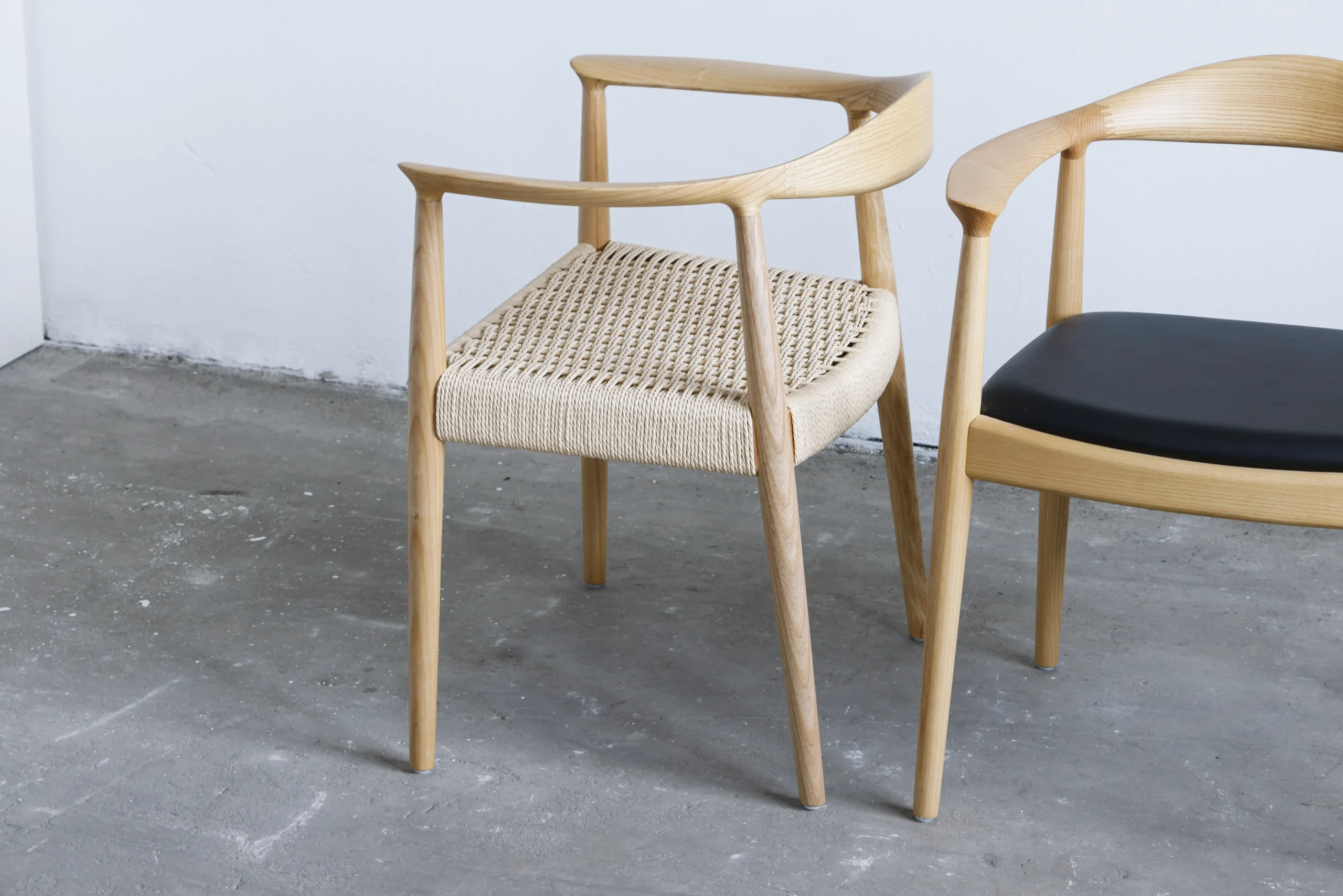 Photo of two Hans Wegner Round Chairs placed together, one featuring a paper rope seat and the other with a microfiber seat, showcasing the contrast between natural and modern materials in iconic design pieces.