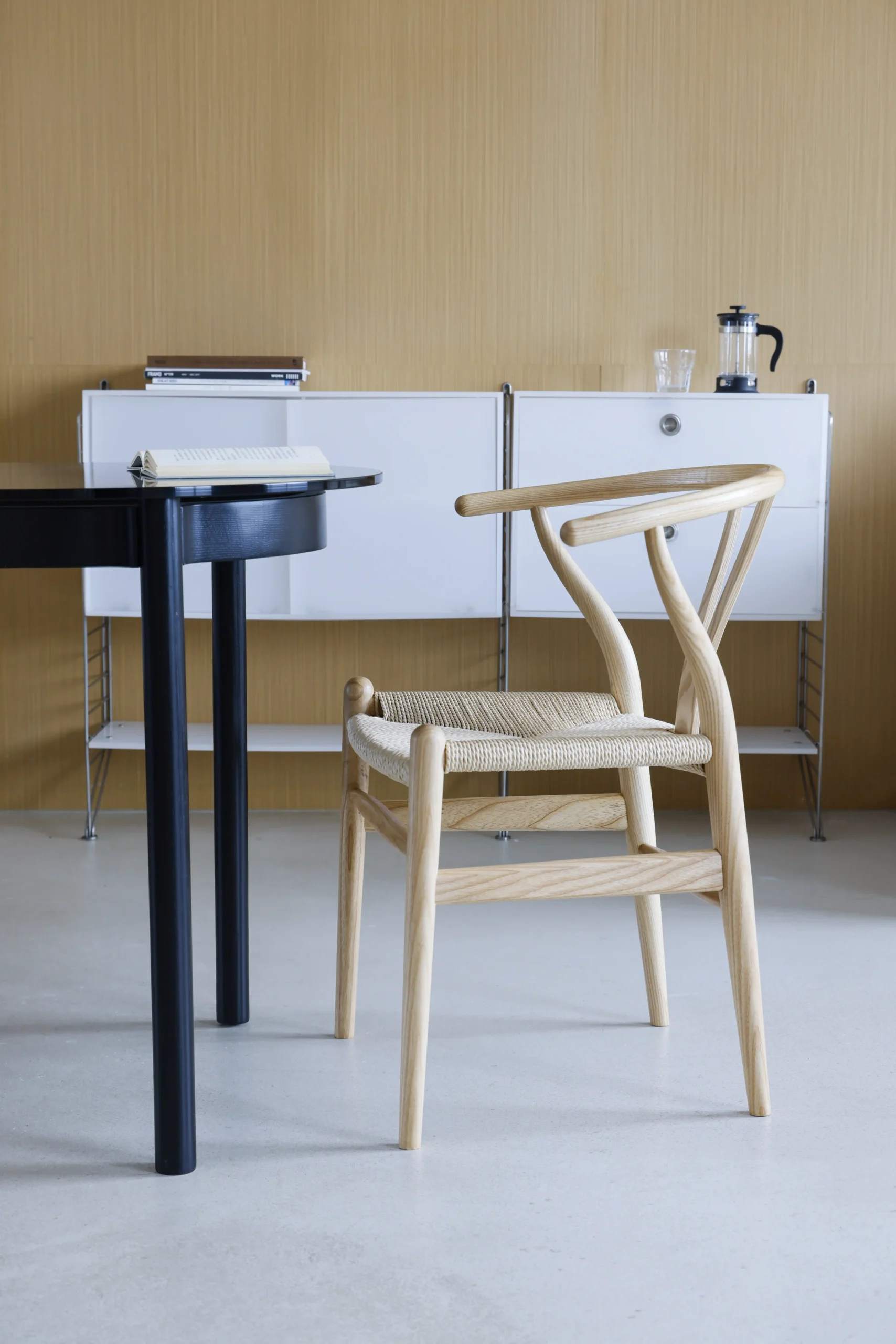 Photo of Hans Wegner's Wishbone Chair in a natural colour, placed in a dining room, highlighting its timeless design and natural aesthetic, blending seamlessly into the modern dining space.