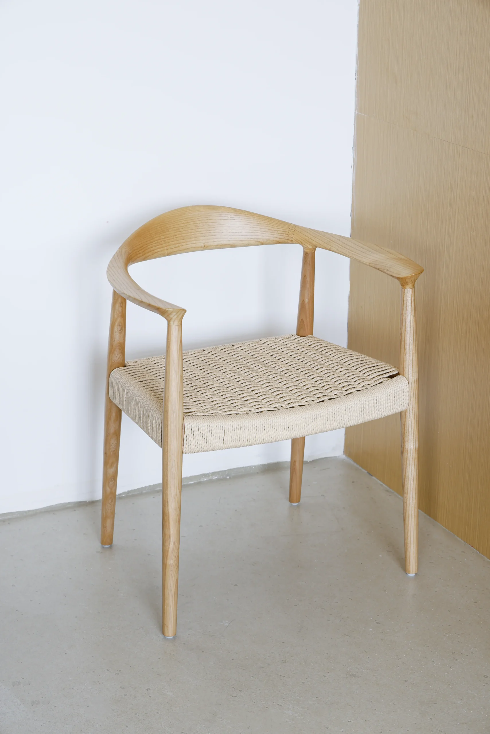 Photo of Hans Wegner's Round Chair with a paper rope seat, placed in the corner of a room, showcasing the chair's natural materials and elegant craftsmanship in a serene interior setting.