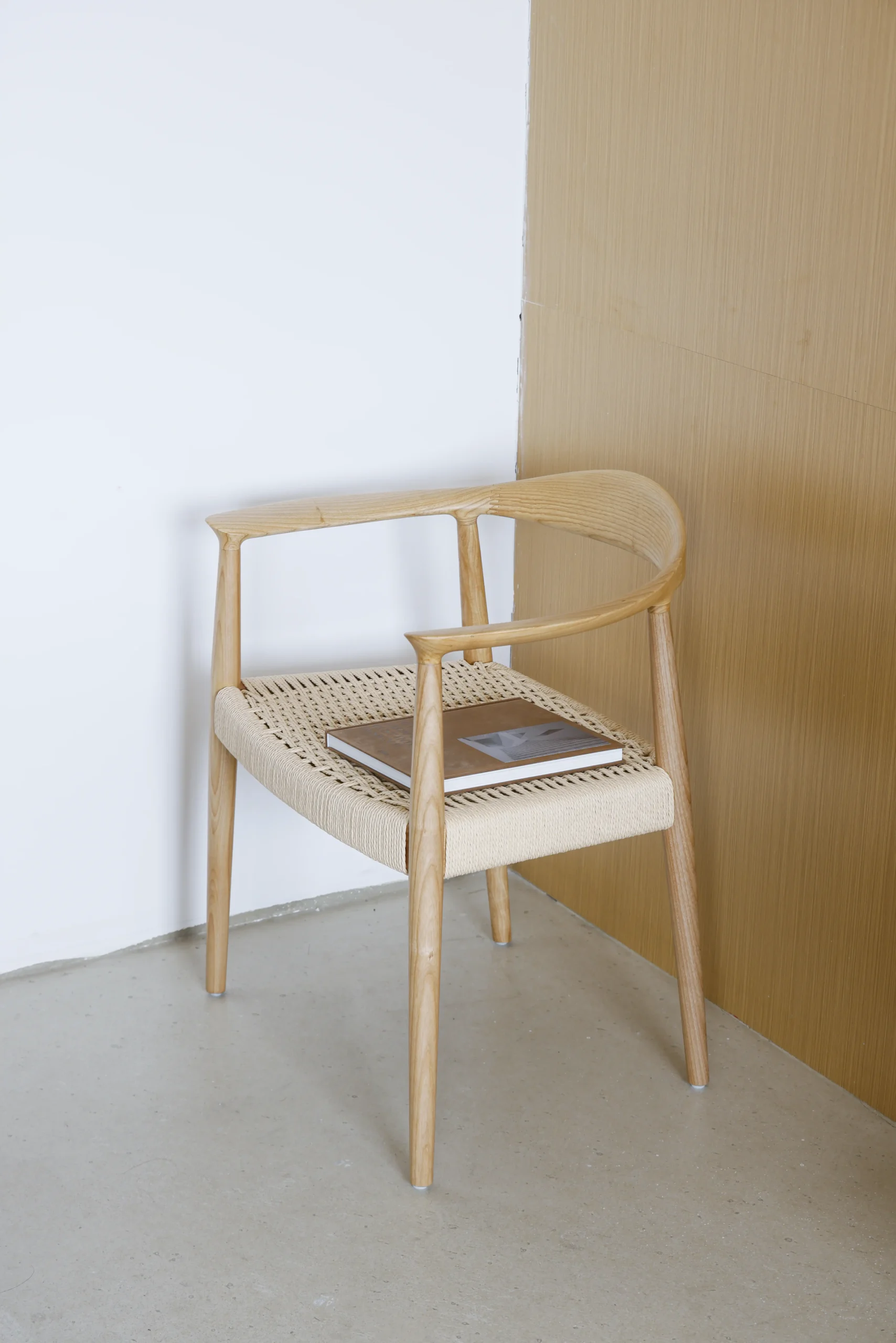 Photo of Hans Wegner's Round Chair with a paper rope seat, placed in the corner of a room, showcasing the chair's natural materials and elegant craftsmanship in a serene interior setting.