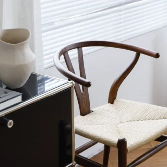 Hans Wegner's Wishbone chair in dark brown, placed near a window in a beautifully lit room setting, emphasizing the blend of natural light and elegant designer timber furniture.