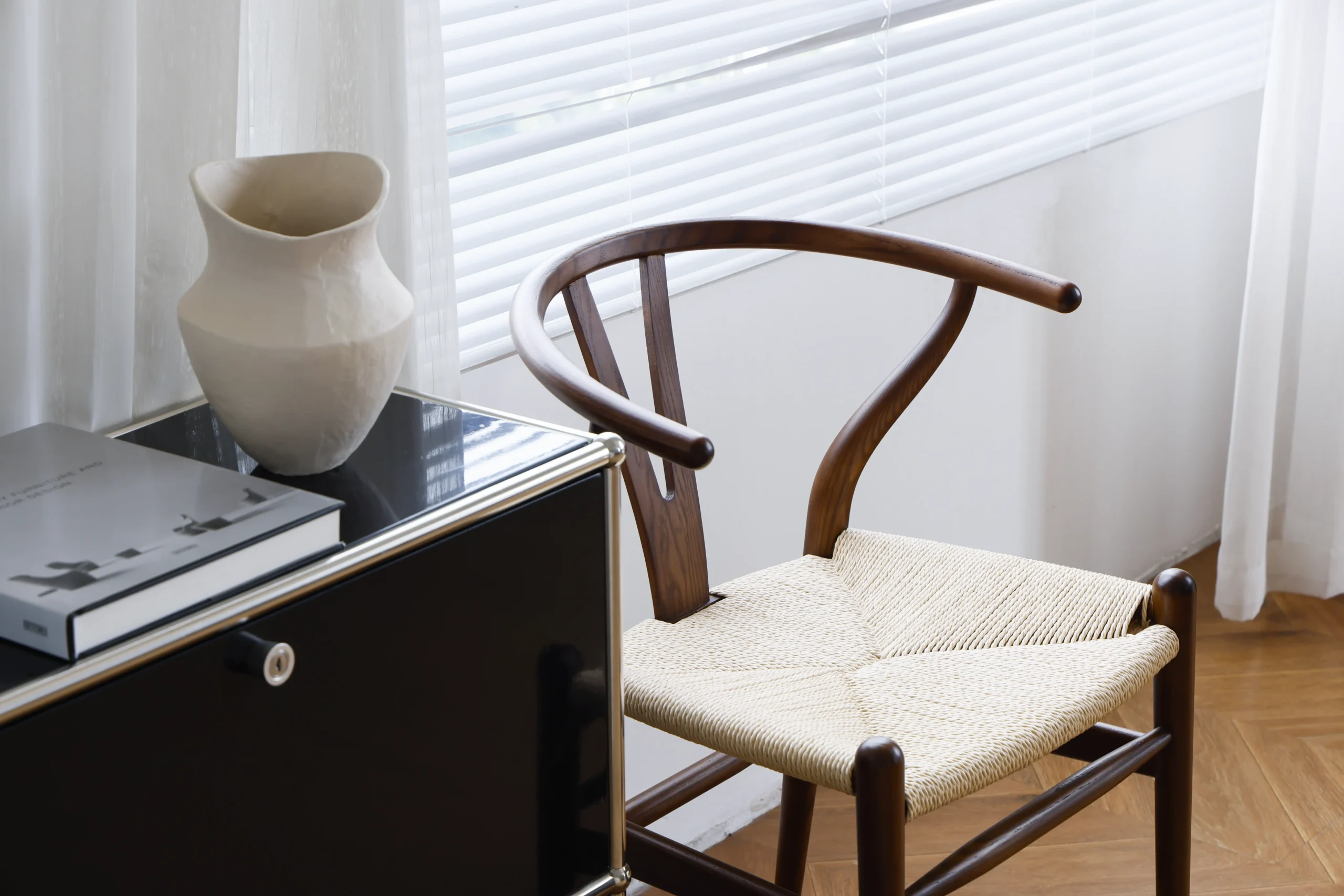 Hans Wegner's Wishbone chair in dark brown, placed near a window in a beautifully lit room setting, emphasizing the blend of natural light and elegant designer timber furniture.