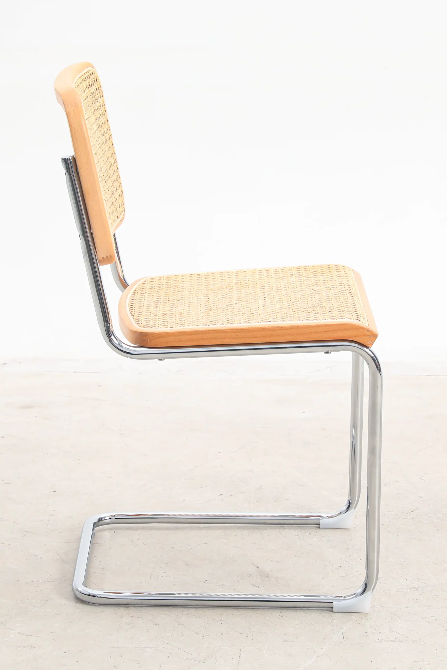 Photo of Marcel Breuer's B32 Cesca Chair from the side view, emphasizing the chair's distinctive cantilevered design, tubular steel frame, and woven cane seat and backrest, representing a hallmark of modernist furniture.