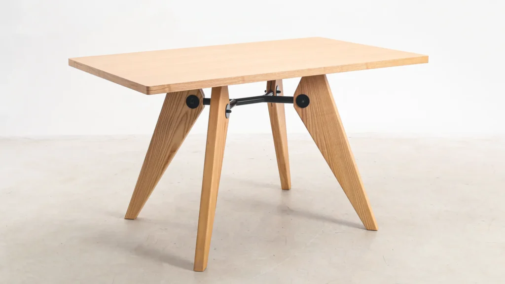 A modern wooden table with a rectangular top and four angled, triangular legs joined by black metal fittings, set against a plain white background.