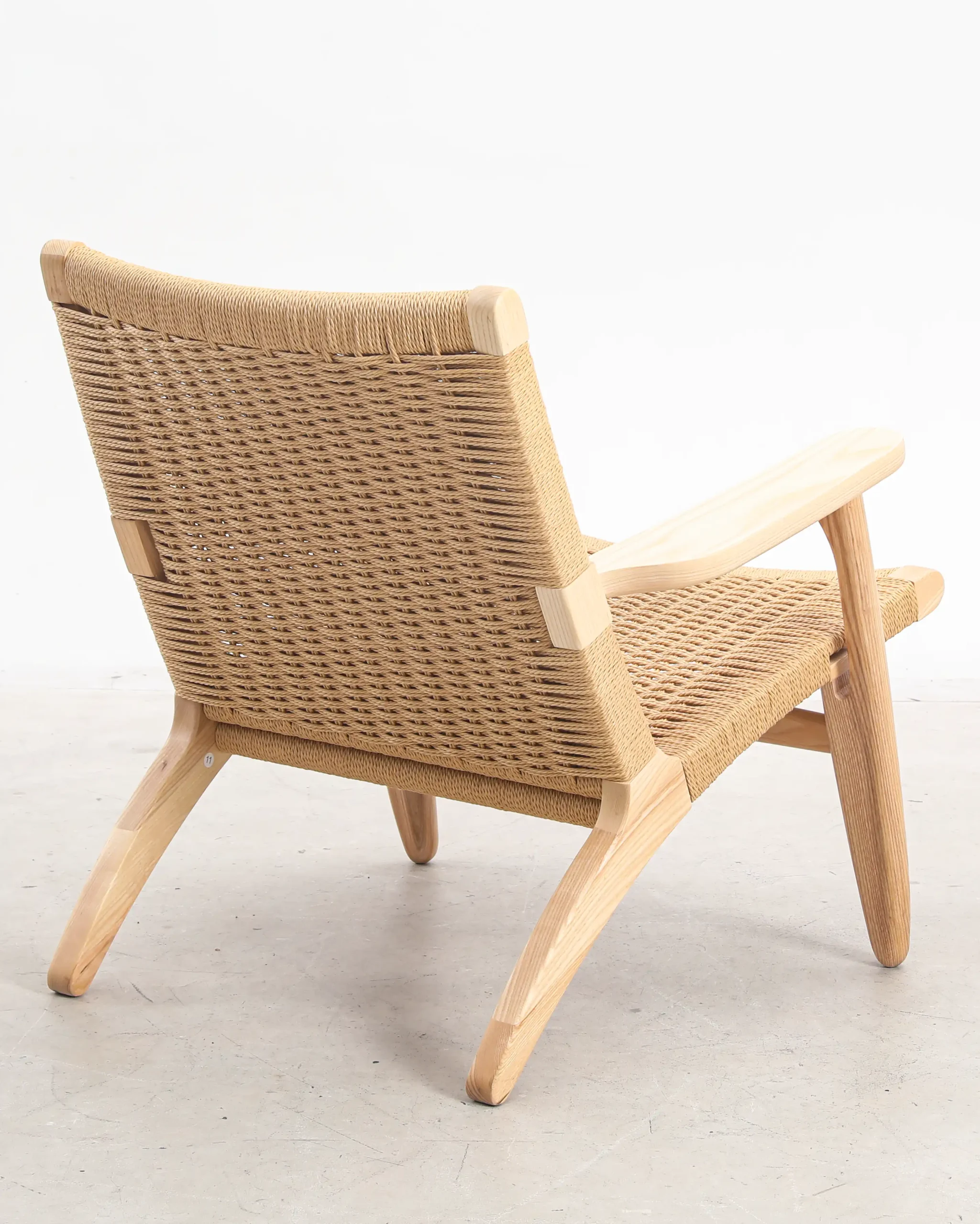 Photo of Hans Wegner's CH25 Easy Chair from the back, highlighting the woven paper cord backrest and the chair's elegant, handcrafted design.