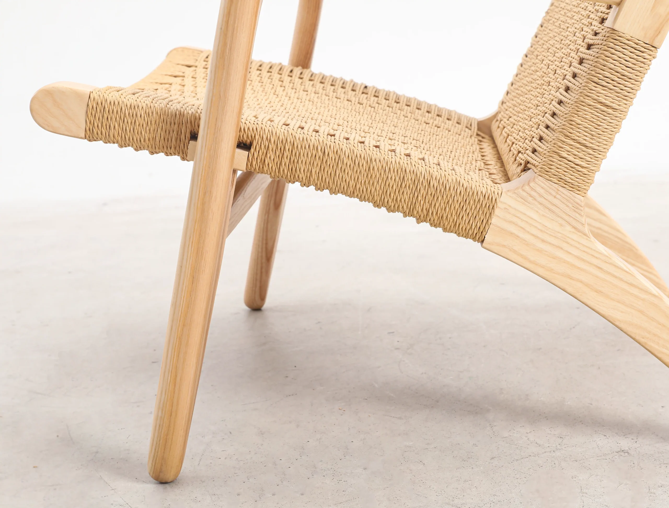 Close-up photo of the lower detail of Hans Wegner's CH25 Easy Chair, showcasing the fine craftsmanship and woven seat that highlight its iconic mid-century design.