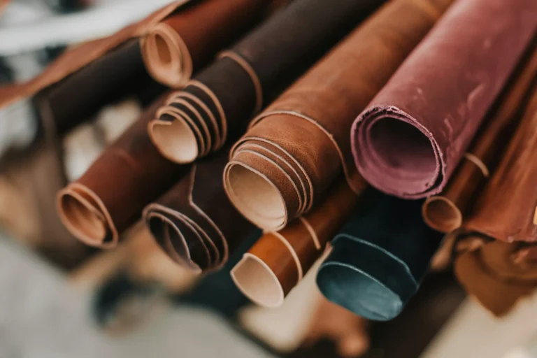 Close-up of several rolls of leather in various shades of brown and burgundy, arranged side by side with the ends facing the camera, showing the texture and layers of the material.