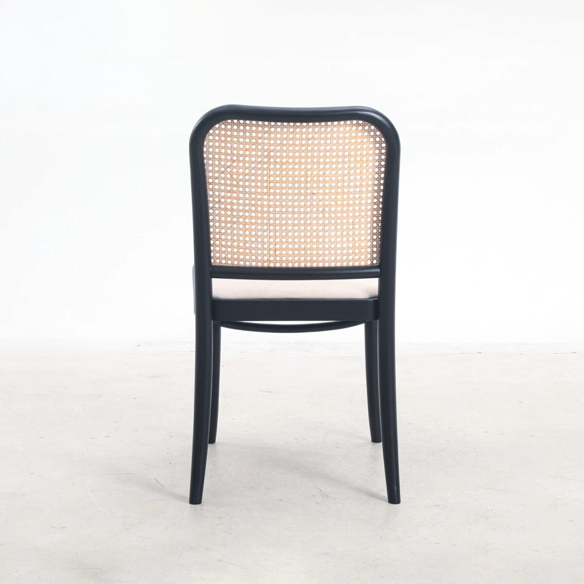 Fabric_B2 A wooden chair with a black frame and a woven cane backrest, viewed from behind, set against a plain white background.