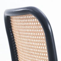 Close-up of a chair back with a black wooden frame and woven cane webbing, set against a white background. The curved top edge and the light texture of the cane are clearly visible.