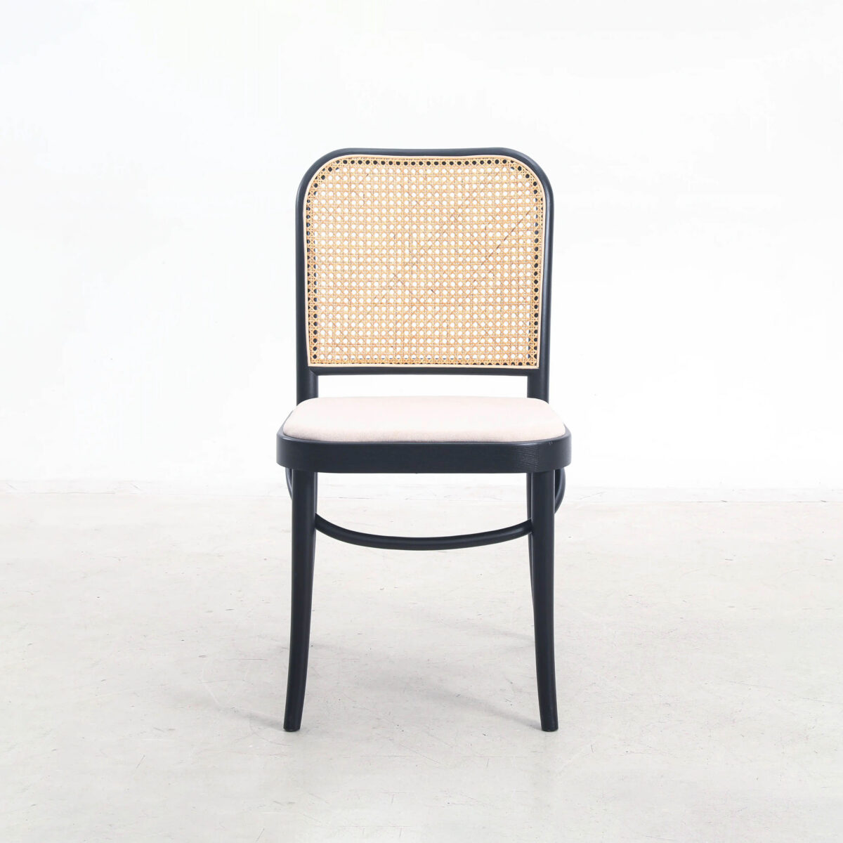 Fabric_B8 A wooden chair with a black frame, a woven cane backrest, and a light-coloured cushioned seat, positioned on a plain light floor against a white background.