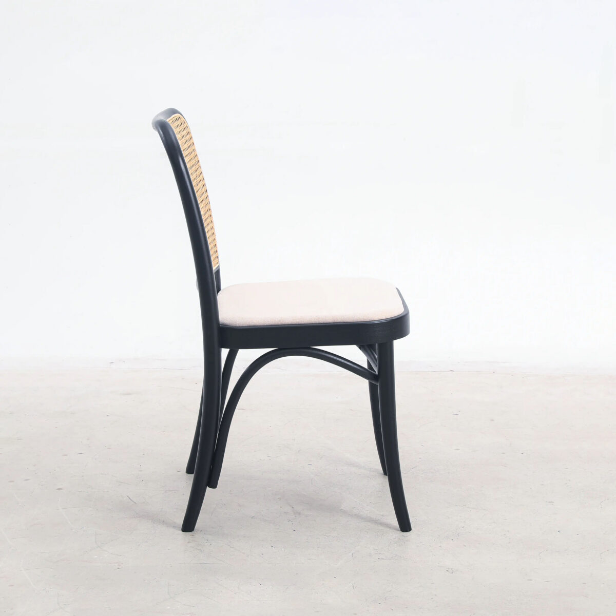 Fabric_B9 A wooden chair with a curved black frame, a woven rattan backrest, and a light beige cushioned seat, shown in profile against a plain white background.